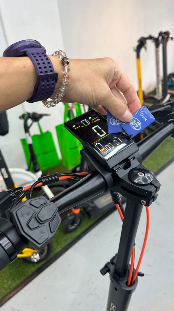 A close-up of a person's hand inserting a NFC card into the control panel of a black JOYOR S5Z electric scooter at Revolt Petaling Jaya, with other scooters visible in the background.